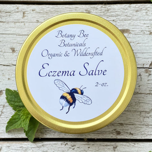 Eczema salve container with gold lid and bee illustration on a wooden surface