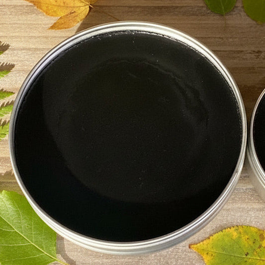 Close-up of a container with Black Drawing Salve on a wooden surface with leaves.