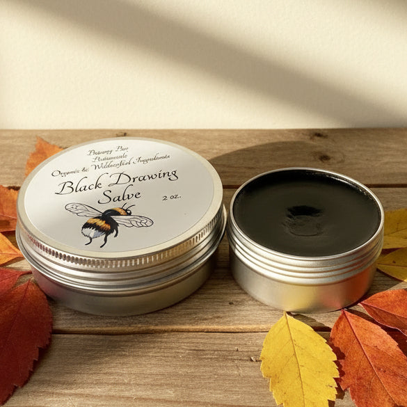 Black Drawing Salve in a metal tin with a label on a wooden surface