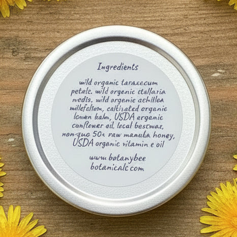 Salve lid with ingredient list on a wooden surface with yellow flowers