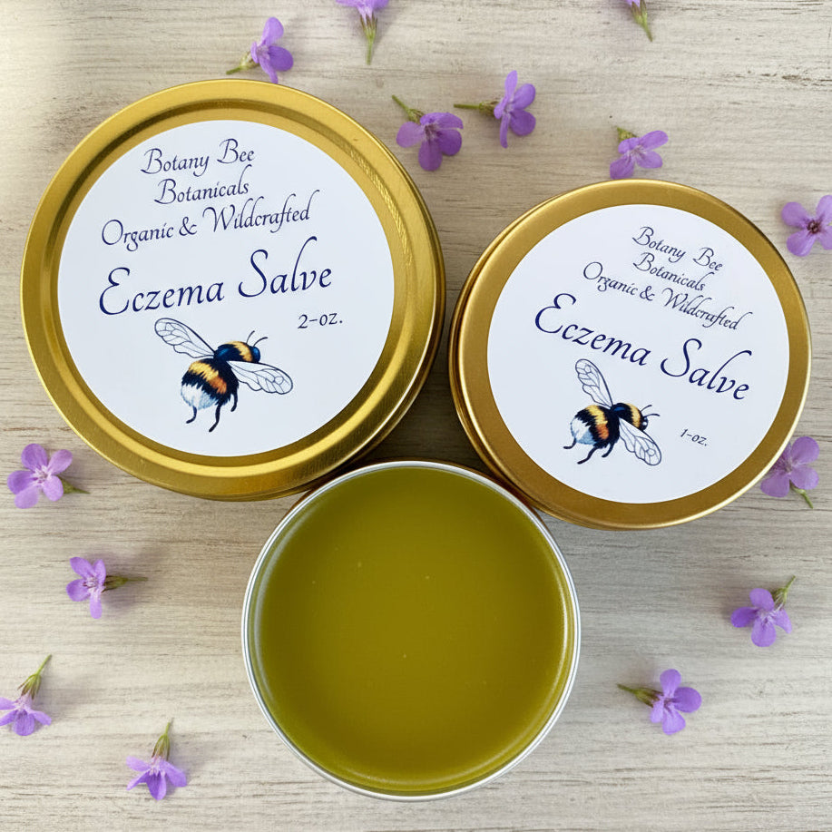 Two tins of Eczema Salve with a small container of green salve on a wooden surface.
