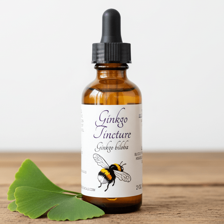 An amber glass dropper bottle labeled 'Ginkgo Tincture Ginkgo biloba' with a black dropper cap, standing on a wooden surface against a light background, with green ginkgo leaves placed beside it.