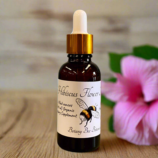 Bottle of Hibiscus Flower tincture with a bee illustration on a label, placed on a wooden surface.