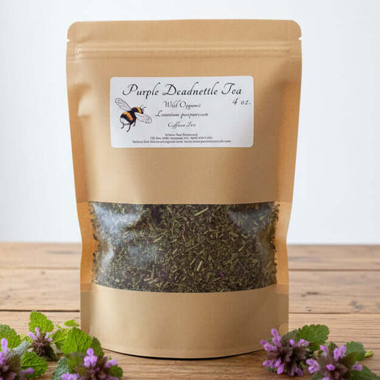Bag of Purple Deadnettle Tea on a wooden table with a person and cabinet in the background.