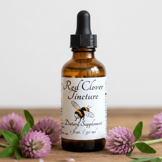 An amber glass dropper bottle labeled 'Red Clover Tincture' stands on a wooden surface with pink clover flowers around it against a light neutral background.