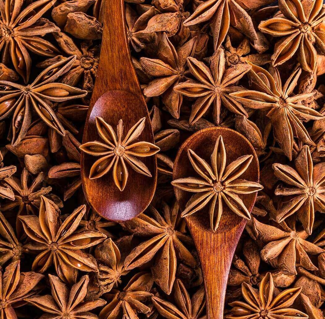 Close-up of whole star anise spices filling the frame, with two wooden spoons resting on top to highlight the star-shaped seeds.