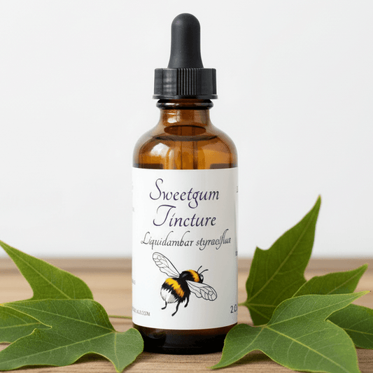 An amber glass dropper bottle labeled 'Sweetgum Tincture' with a black cap, styled with green leaves on a wooden surface against a white background.