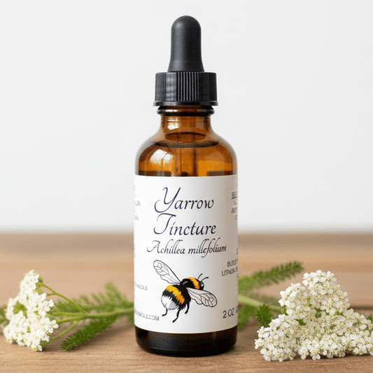 An amber glass dropper bottle labeled 'Yarrow Tincture' with a black cap, set on a wooden surface with white yarrow flowers on both sides.